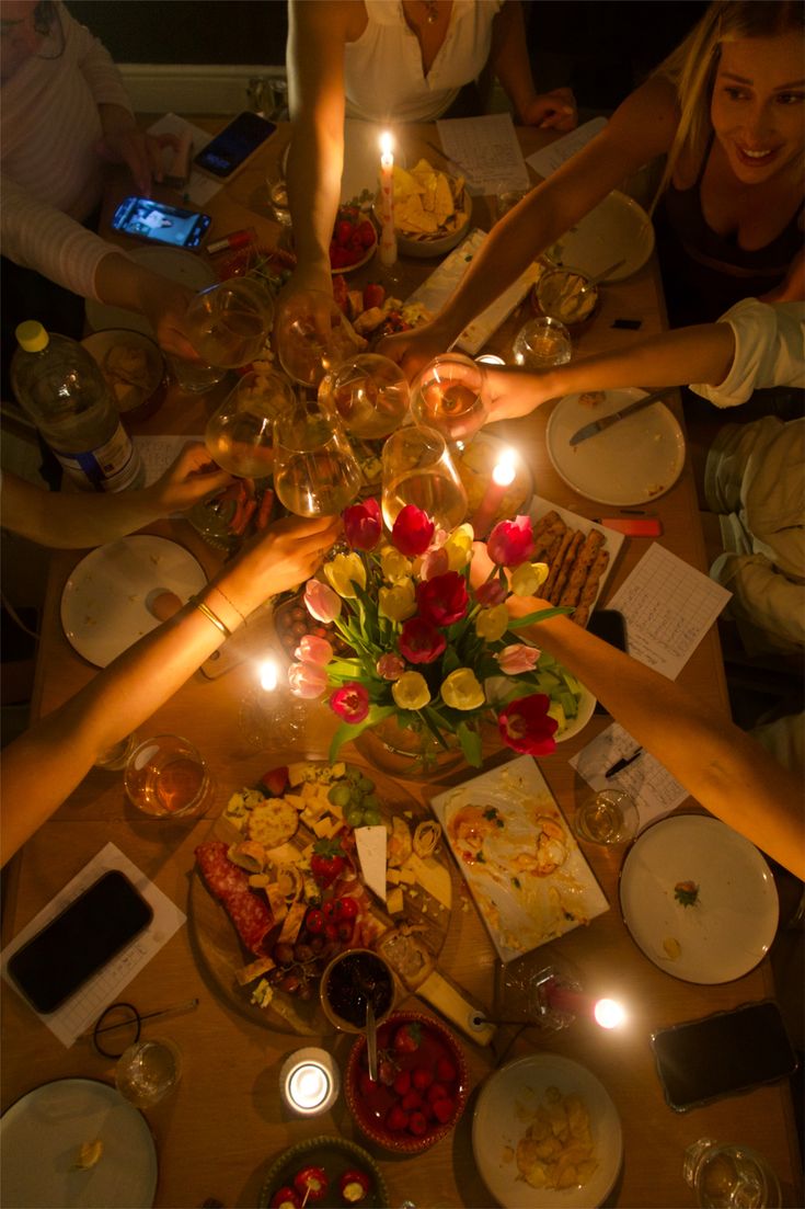 Hands toasting over a candlelit dinner spread